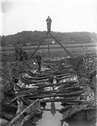 På detta fotografi är vi närvarande vid utgrävningen av Sveriges första bevarade vikingaskepp, Äskekärrskeppet. Skeppet användes till handel och frakt, kallat för knarr. En man vid namn Otto Karlén upptäckte delar av farkosten i samband med en utgrävning i Äskekärr i Ale kommun i Västergötland i början av 1900-talet, exakt årtal är okänt. Karlén tyckte inte att fyndet var märkvärdigt och det hela föll i glömska. 1933 hittade markägaren John Antonsson fyndet på nytt och valde att rapportera upptäckten. Knarren är daterat till 830-talet, den är cirka 16 meter lång, cirka 4,6 meter bred och är klinkbyggd. Klink är en metod där man, enkelt förklarat, lägger brädorna i omlott så att varje brädas underkant vilar utanför den bräda som ligger nedanför i bordläggningen, båtens yttre skal. Klinkmetoden härstammar från Skandinavien och i december 2021 skrevs denna skandinaviska byggtradition in på UNESCOs lista över immateriella kulturarv. Detta är något jag tycker att vi skandinaver borde vara mycket stolta över. I dag finns Äskekärrskeppet utställt hos Göteborgs stadsmuseum. Kilde: Kalla Norden på Facebook 2022